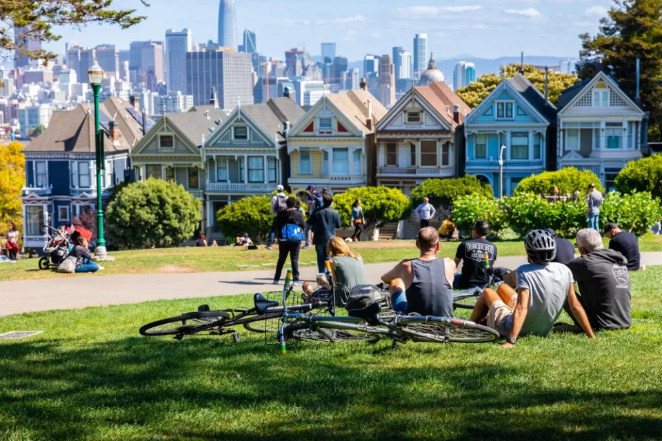 People lounging on grass in Alamo Square park in San Francisco overlooking painted ladies Victorian houses and city skyline